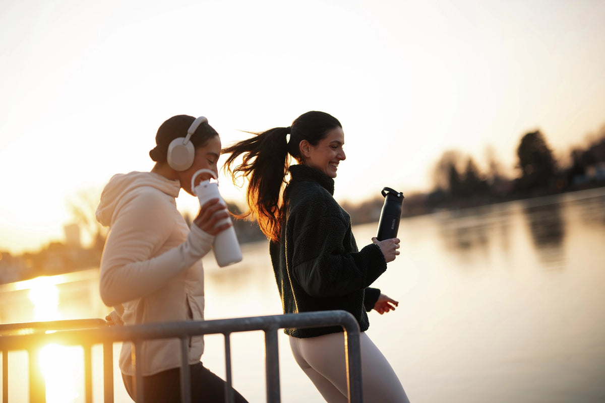 Two people carrying black and white BRITA LARQ bottles while running beside a waterfront.