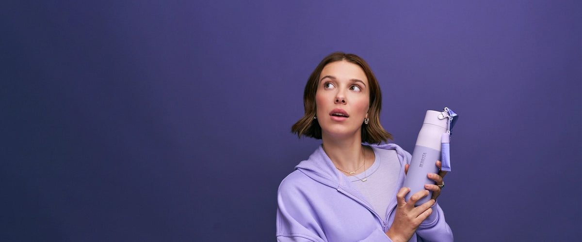 Millie Bobby Brown is holding the florence by mills x BRITA LARQ bottle on purple background.