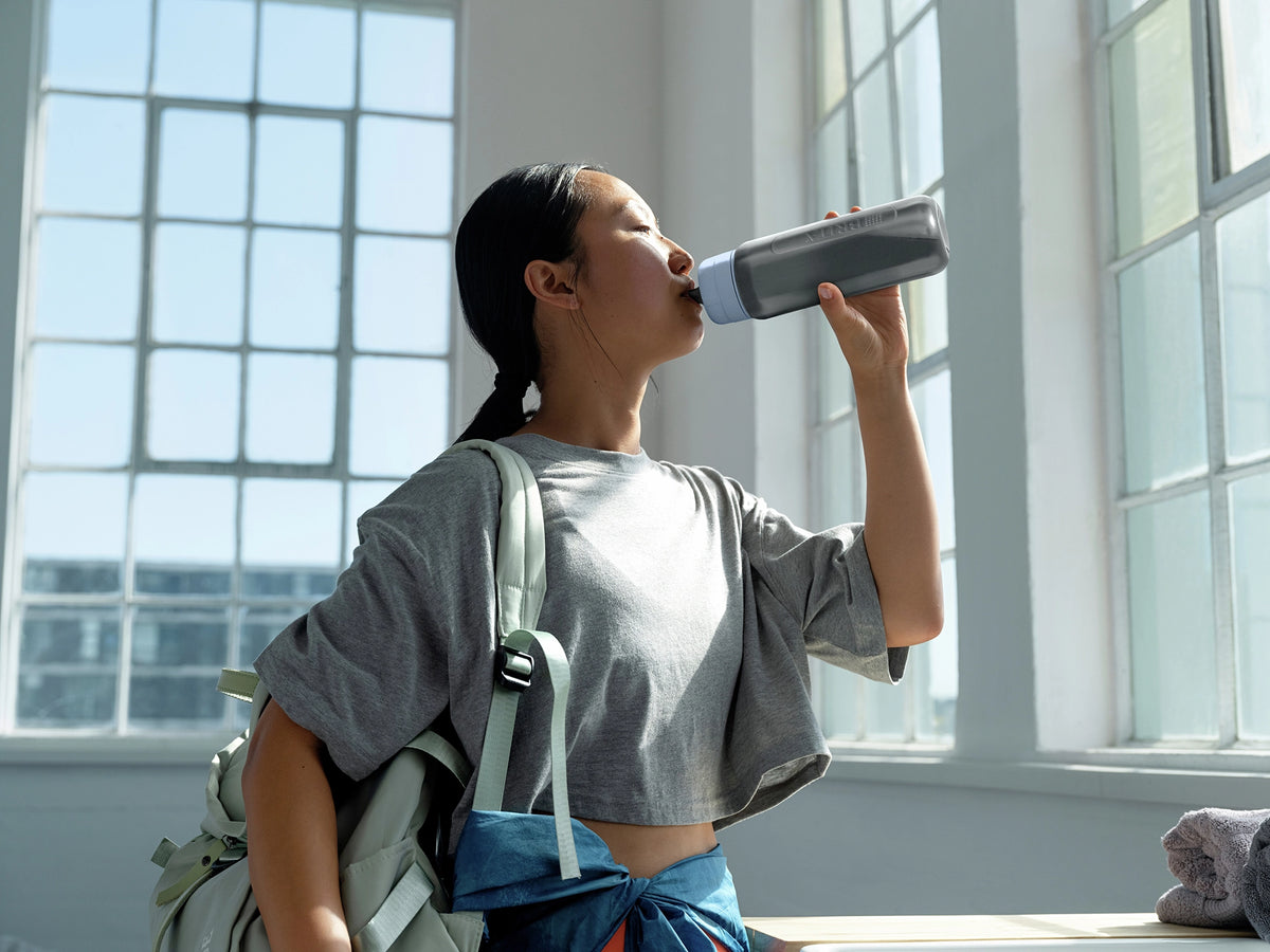Woman drinking from a BRITA water filter bottle Model Active in a bright room with large windows.