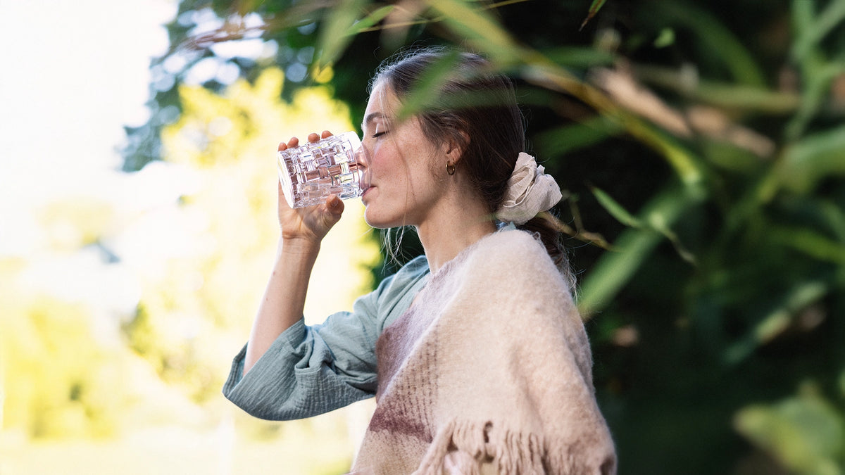 Woman drinking a glass of water sitting in greenery.