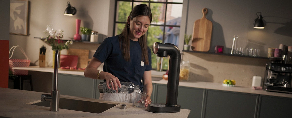 Woman using the BRITA sodaONE Sparkling Water Maker in a modern kitchen.