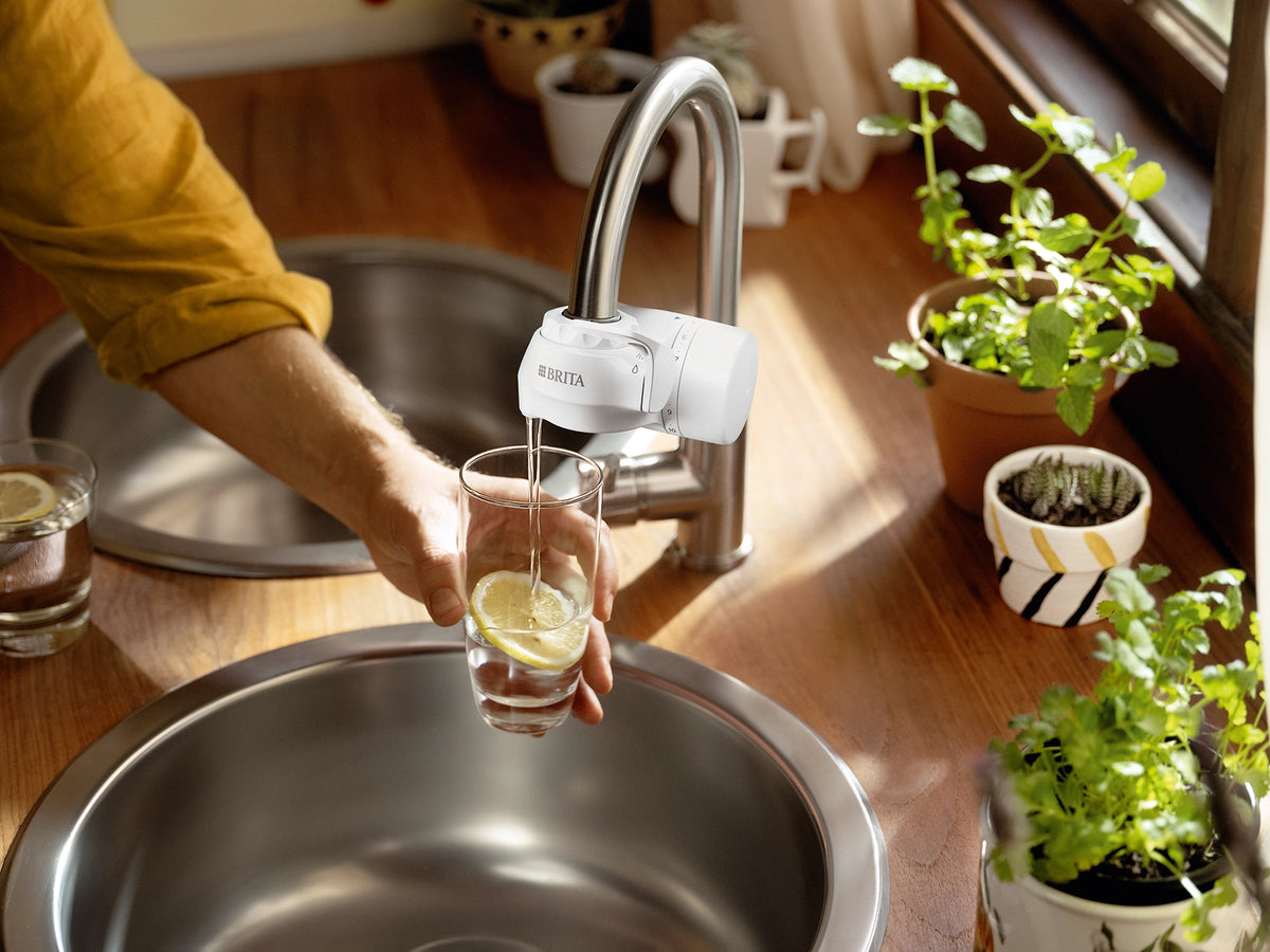 Glass with a lemon slice being filled with filtered water from a BRITA ON TAP water filter system.
